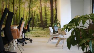 Un espacio de oficina con sillas ergonómicas, una planta grande en maceta y vistas a un bosque a través de una ventana.