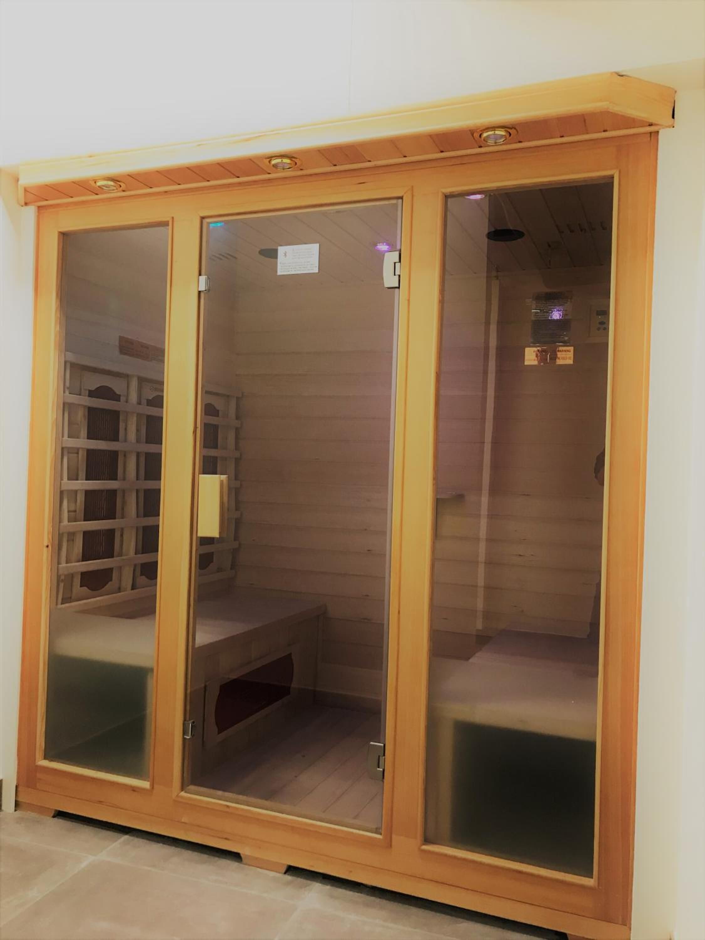 Een houten garderobe met glazen deuren, een bankje binnenin en een klein legplankje.