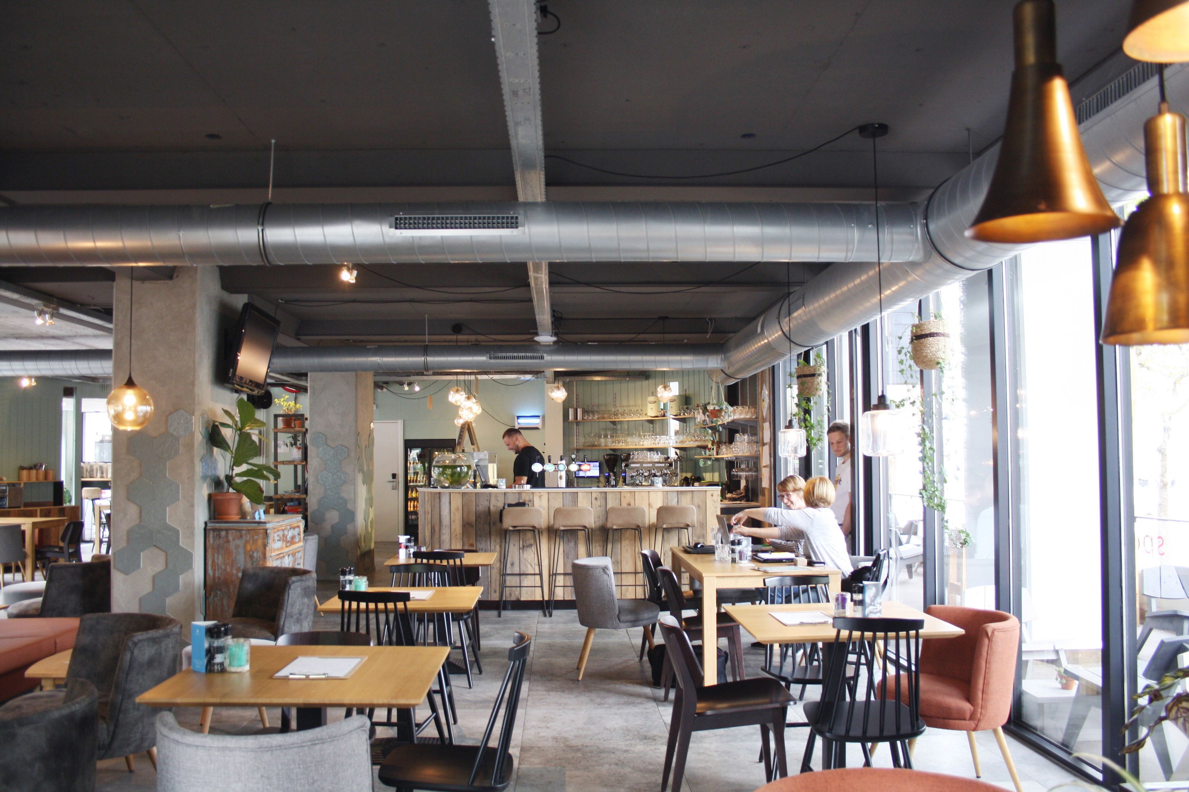 Un café moderno con conductos expuestos, mesas de madera y asientos en la barra.