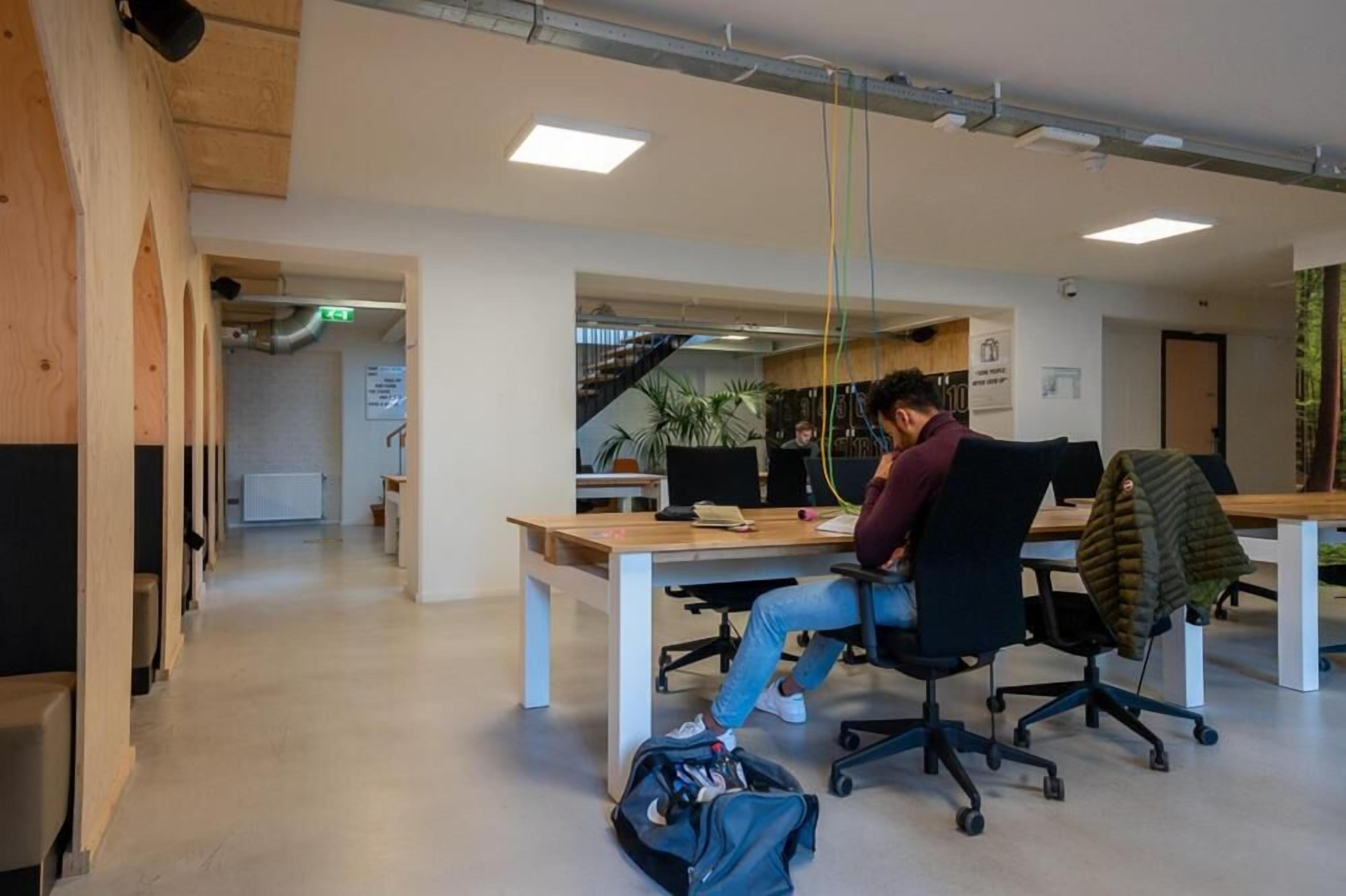 Un bureau avec une personne assise à un bureau, un escalier en arrière-plan et une plante posée sur le bureau.