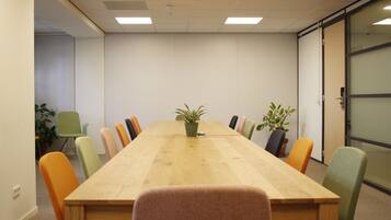 A conference room with a long wooden table, colorful chairs, and potted plants.