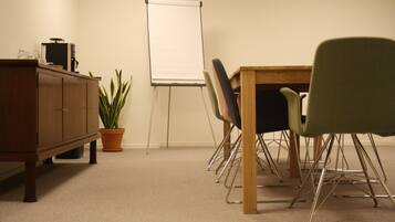 Ein Konferenzraum mit Holztisch, vier Stühlen, einer Whiteboard-Tafel, einer Kaffeemaschine und einem Blumentopf.