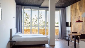 A modern bedroom with a large bed, a dining area, and a view of trees through large windows. - Guesthouse Vertoef (Nijmegen)