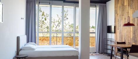 A modern bedroom with a large bed, a dining area, and a view of trees through large windows.