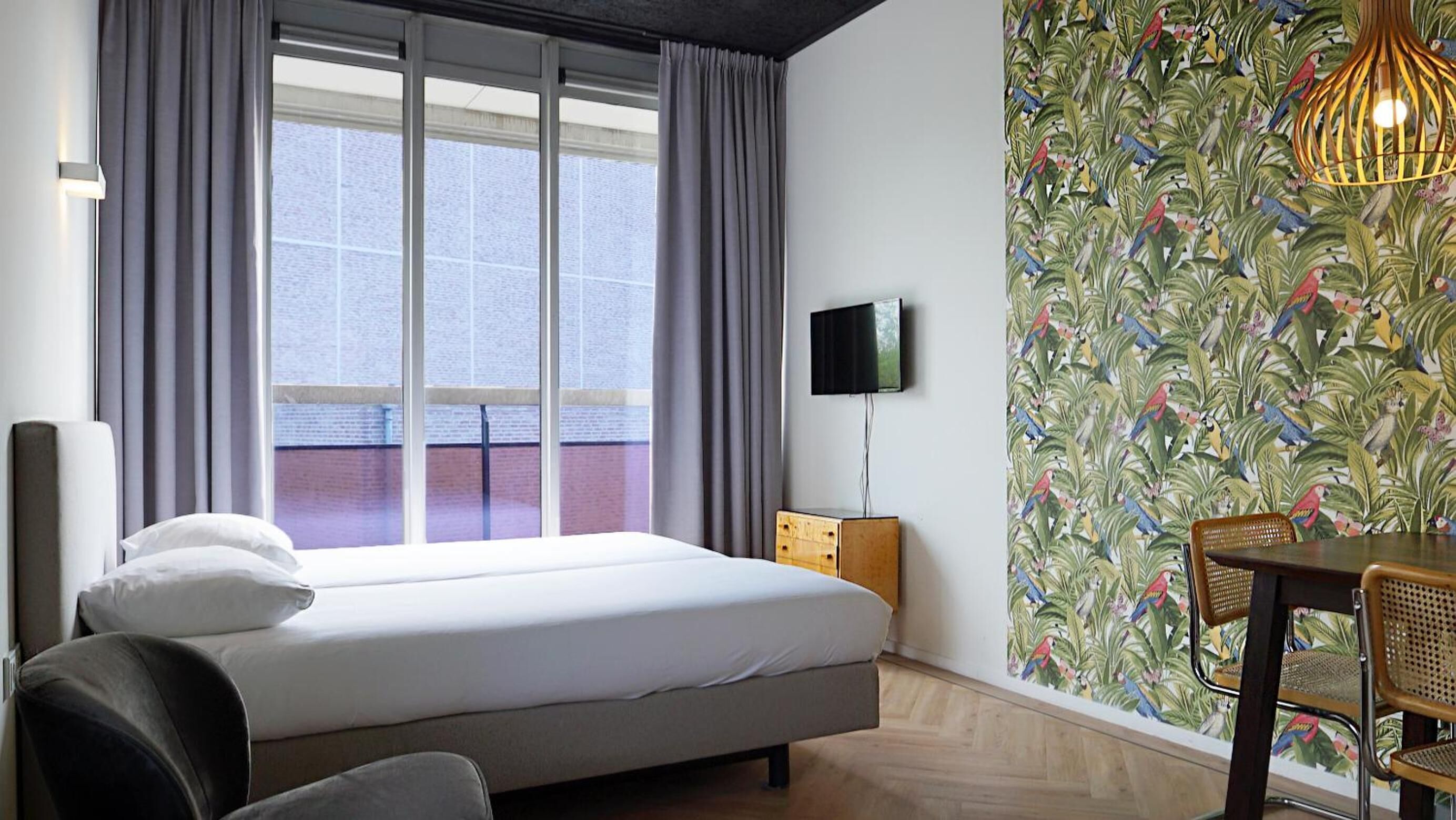 Habitación de hotel con cama, televisión, mesa de comedor con sillas y ventana con cortinas.