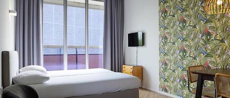 Habitación de hotel con cama, televisión, mesa de comedor con sillas y ventana con cortinas.