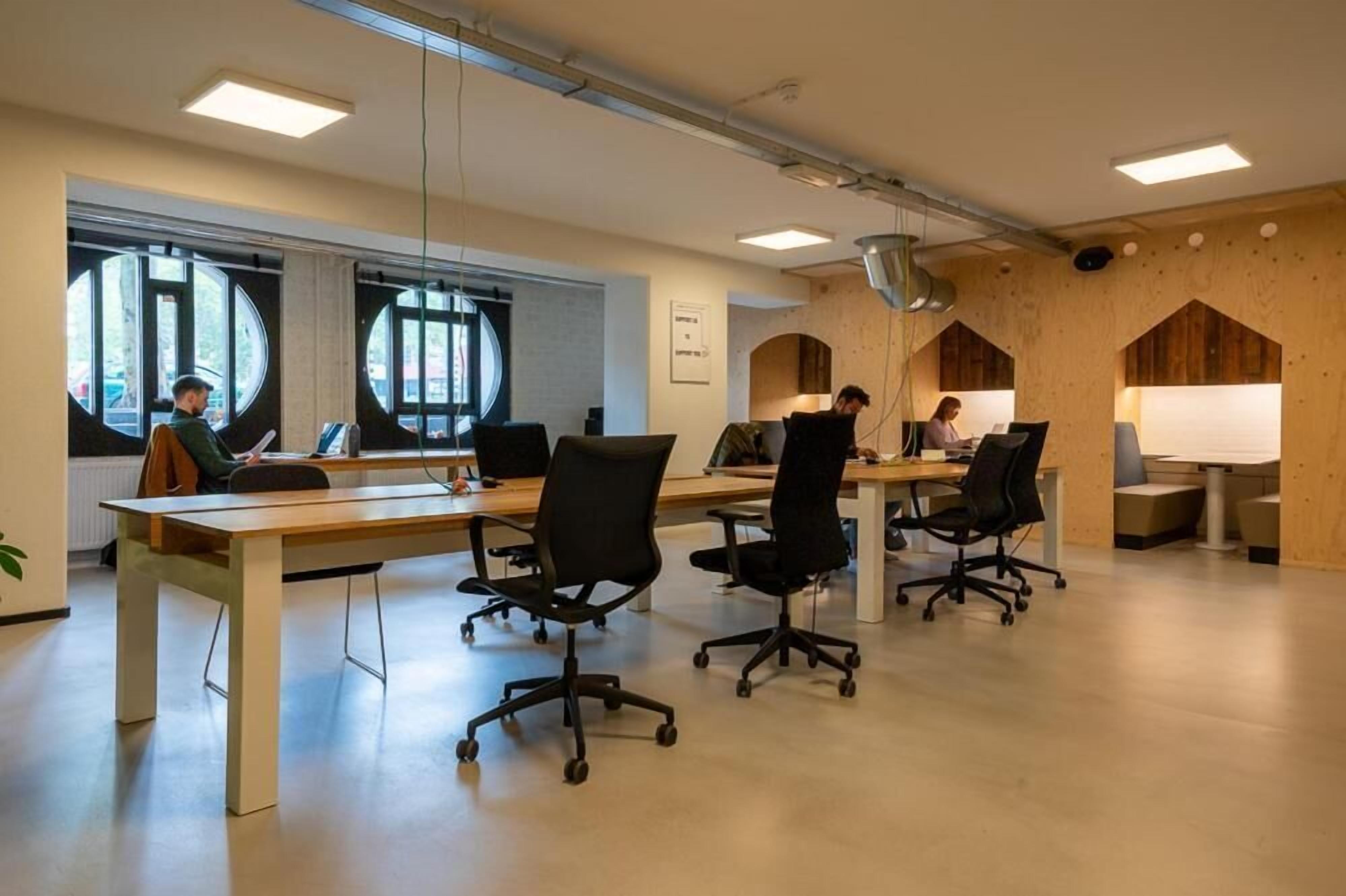 Un espacio de oficina moderno con mesas largas, sillas de oficina negras y ventanas amplias.