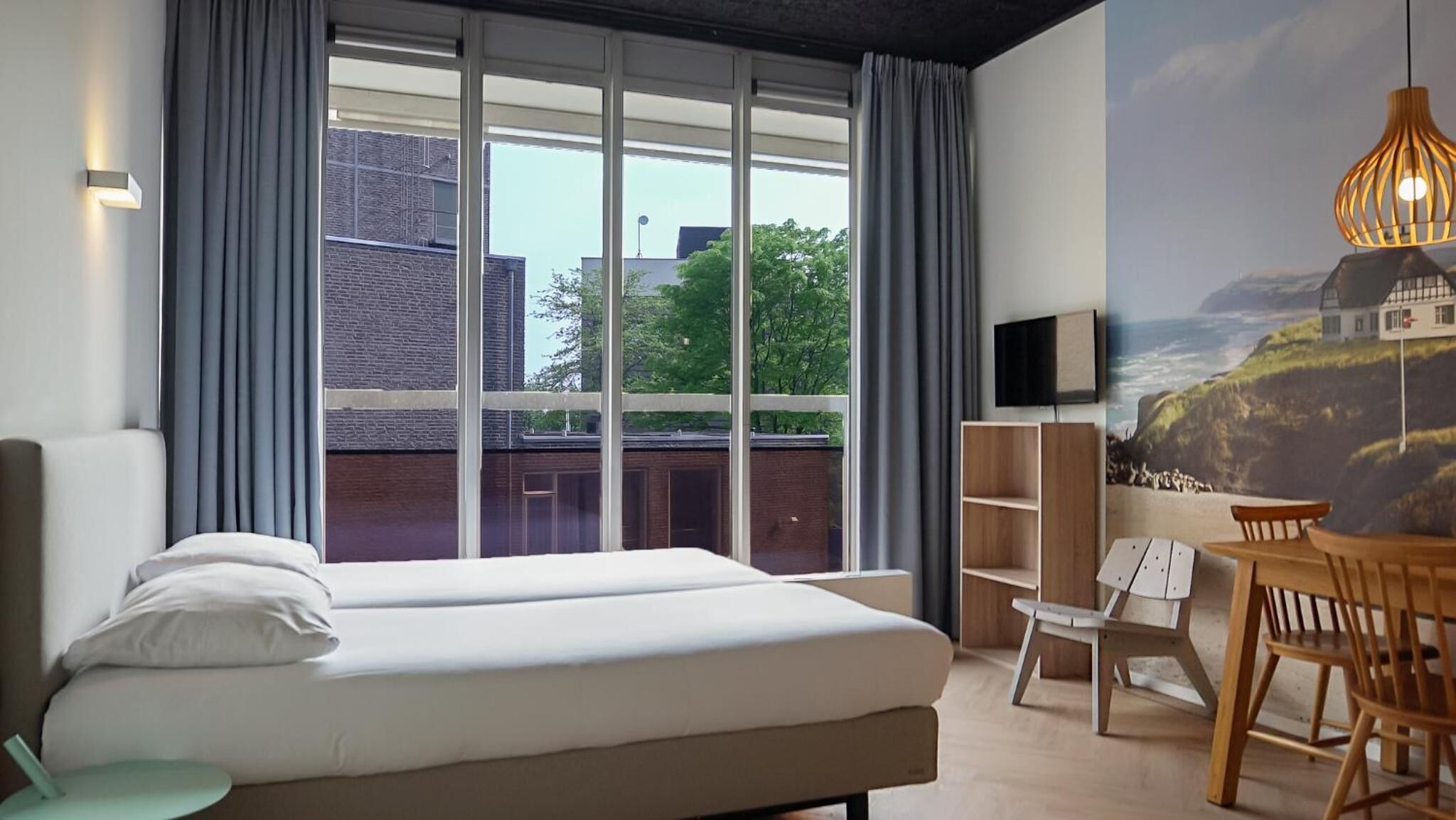 Una habitación de hotel moderna con un ventanal grande, una cama, un escritorio y una silla.