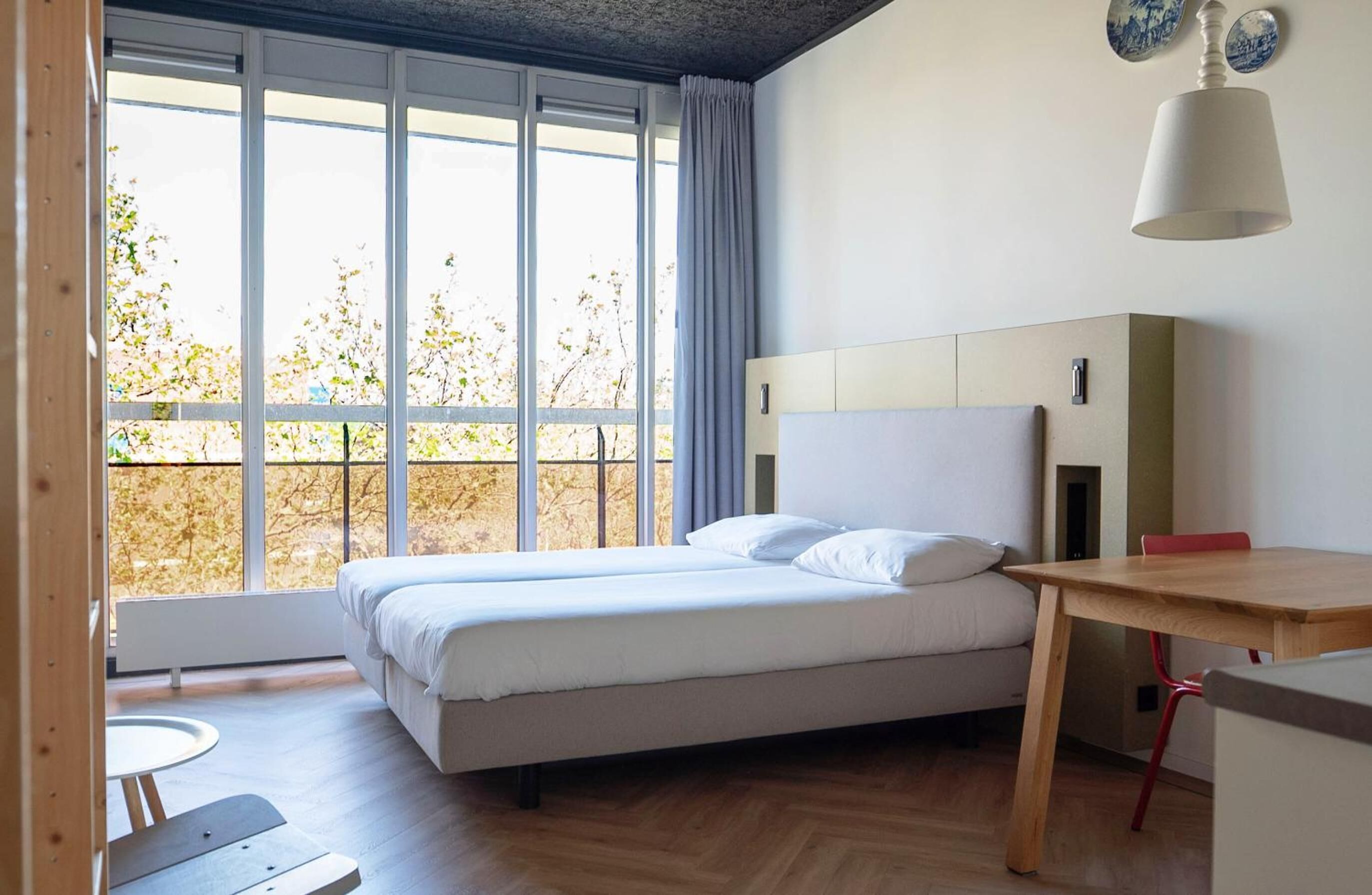 A modern bedroom with a bed, a desk, and a window with a view of trees.