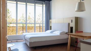 A modern bedroom with a bed, a desk, and a window with a view of trees.