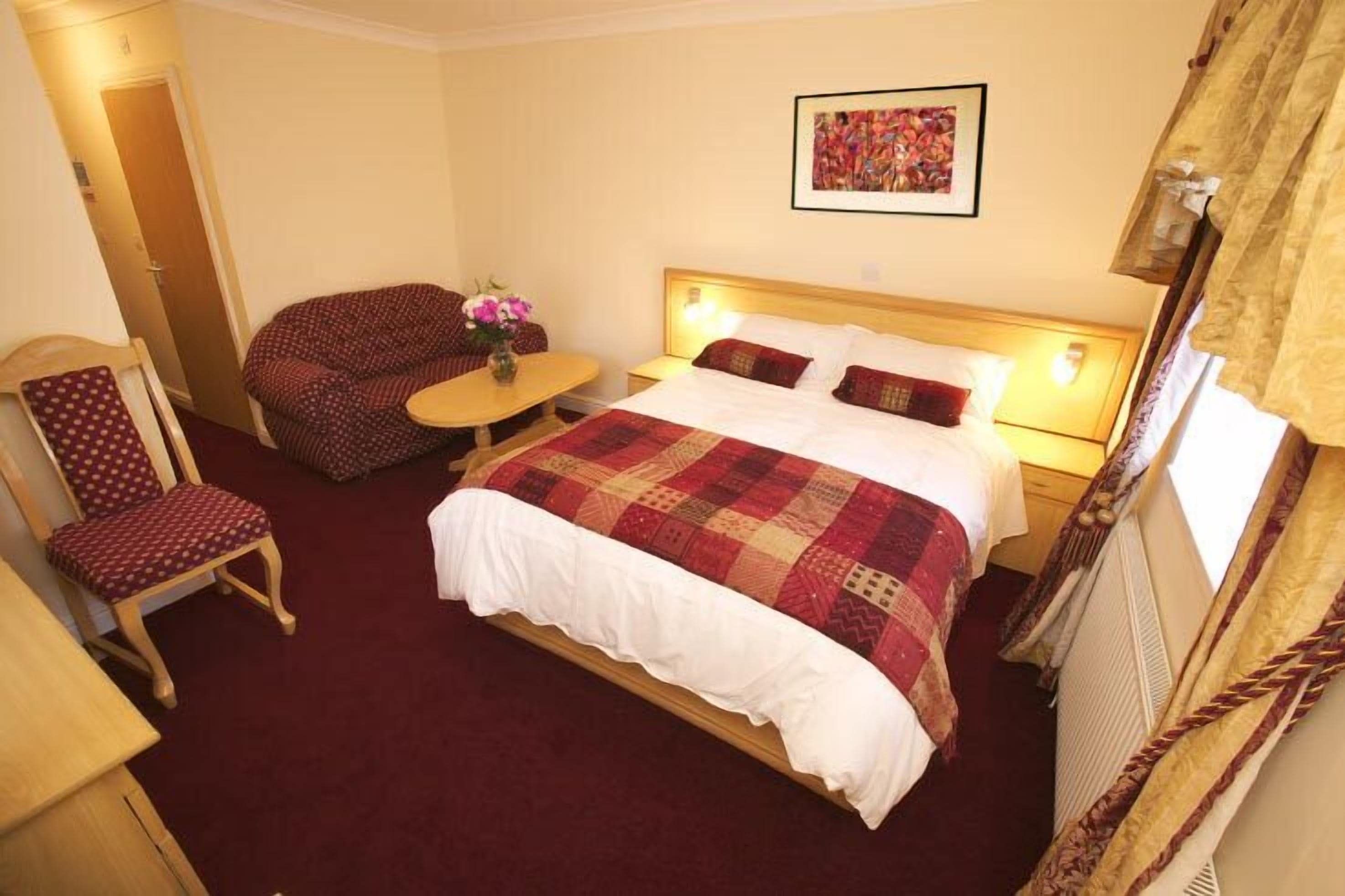 Ein Hotelzimmer mit Bett, Sessel, einem kleinen Tisch mit Blumen und einem Bild an der Wand.