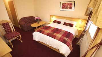 Ein Hotelzimmer mit Bett, Sessel, einem kleinen Tisch mit Blumen und einem Bild an der Wand.