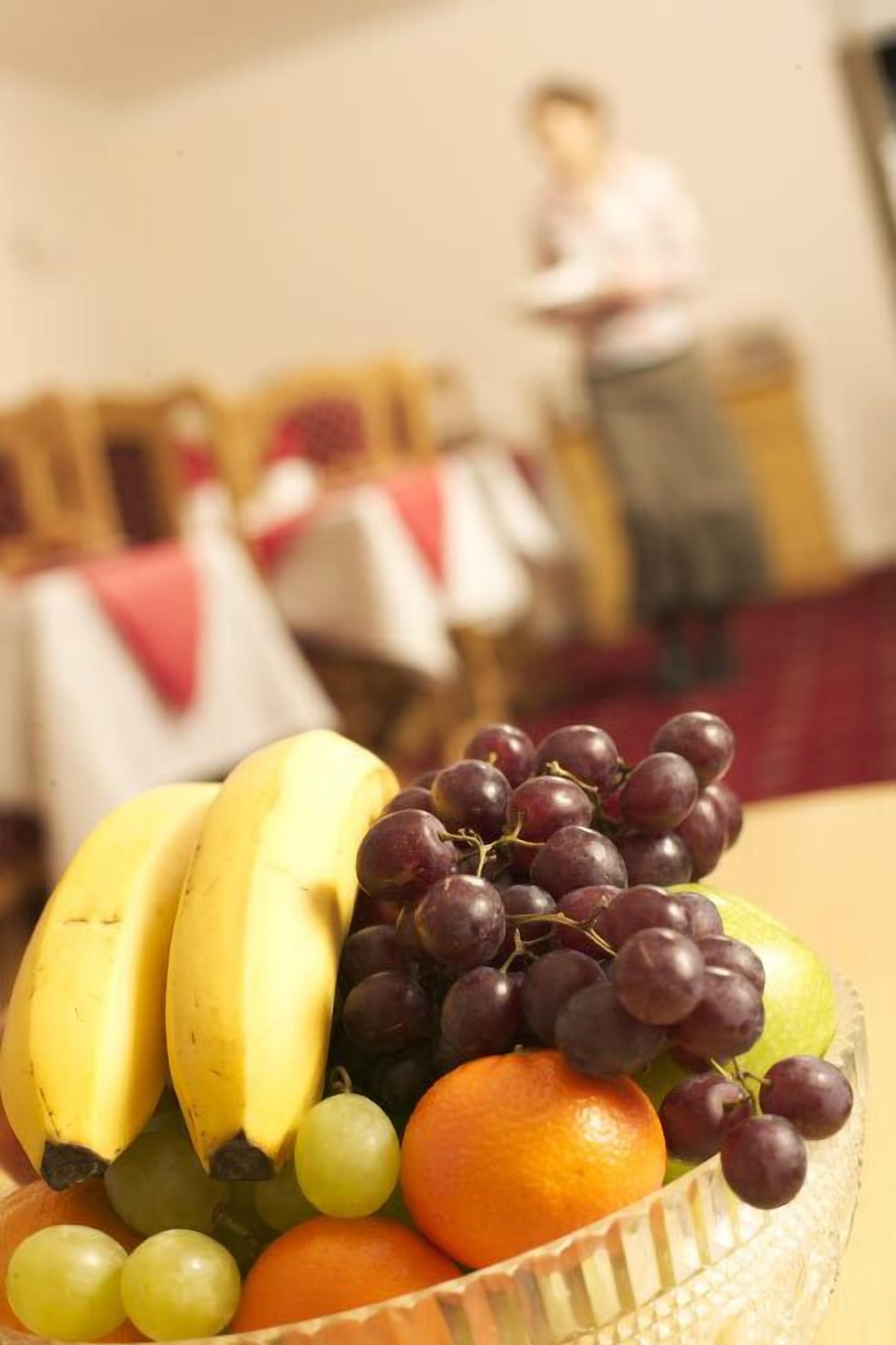 A fruit bowl with bananas, grapes, and an orange on a table.