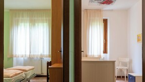 A room with a bed, a desk, and a chair. There is a window with curtains and a radiator. - Casa Lucia 1 - Three Bedroom Apartment, Sleeps 5 (Idro)