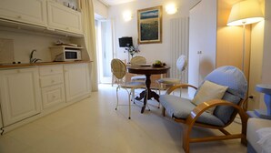 A compact room with a dining table, chairs, a sofa, and a kitchen area with cabinets and a microwave. - Appartamento- Murex - Studio Apartment, Sleeps 3 (Marina di Castagneto Carducci)
