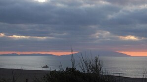 A beach with a boat in the water, a mountain in the distance, and a cloudy sky. - Appartamento- Murex - Studio Apartment, Sleeps 3 (Marina di Castagneto Carducci)