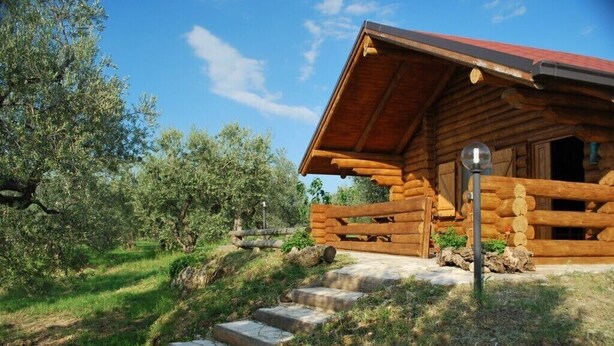 Una cabaña de troncos con fachada de madera, escalones de piedra que conducen a la entrada y un cielo despejado.