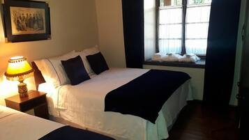 Habitación de hotel con dos camas, una mesita de noche con lámpara, una ventana con cortinas y un cuadro en la pared.