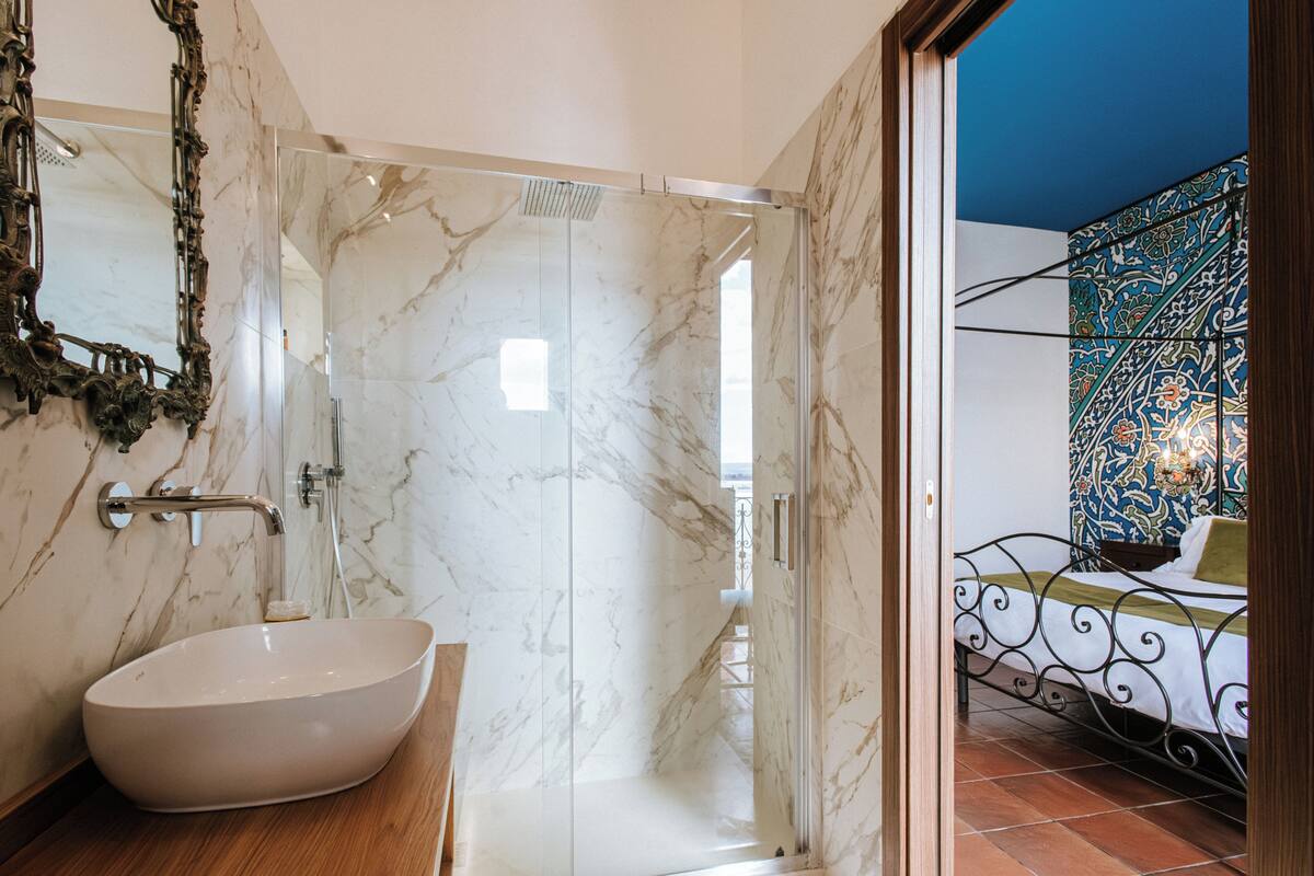 Une salle de bain dotée d’un grand lavabo en marbre, d’une douche en verre et d’un lit avec une tête de lit à motifs.