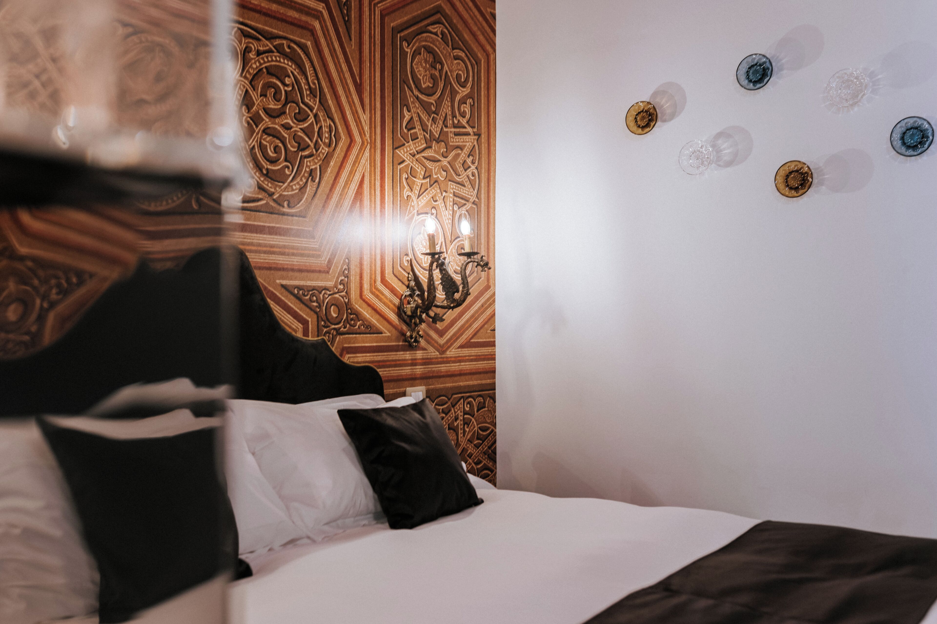 Una habitación de hotel con cama, cabecera de madera, lámpara de pared y panel decorativo.