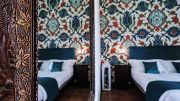 Habitación de hotel con pared espejada, dos camas con cabeceros azules y un papel tapiz estampado.