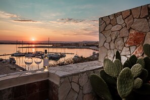 A sunset view from a balcony with a stone wall, cacti, and wine glasses. - Palazzo Giunta - Porta Marina Ortigia  (Syracuse)
