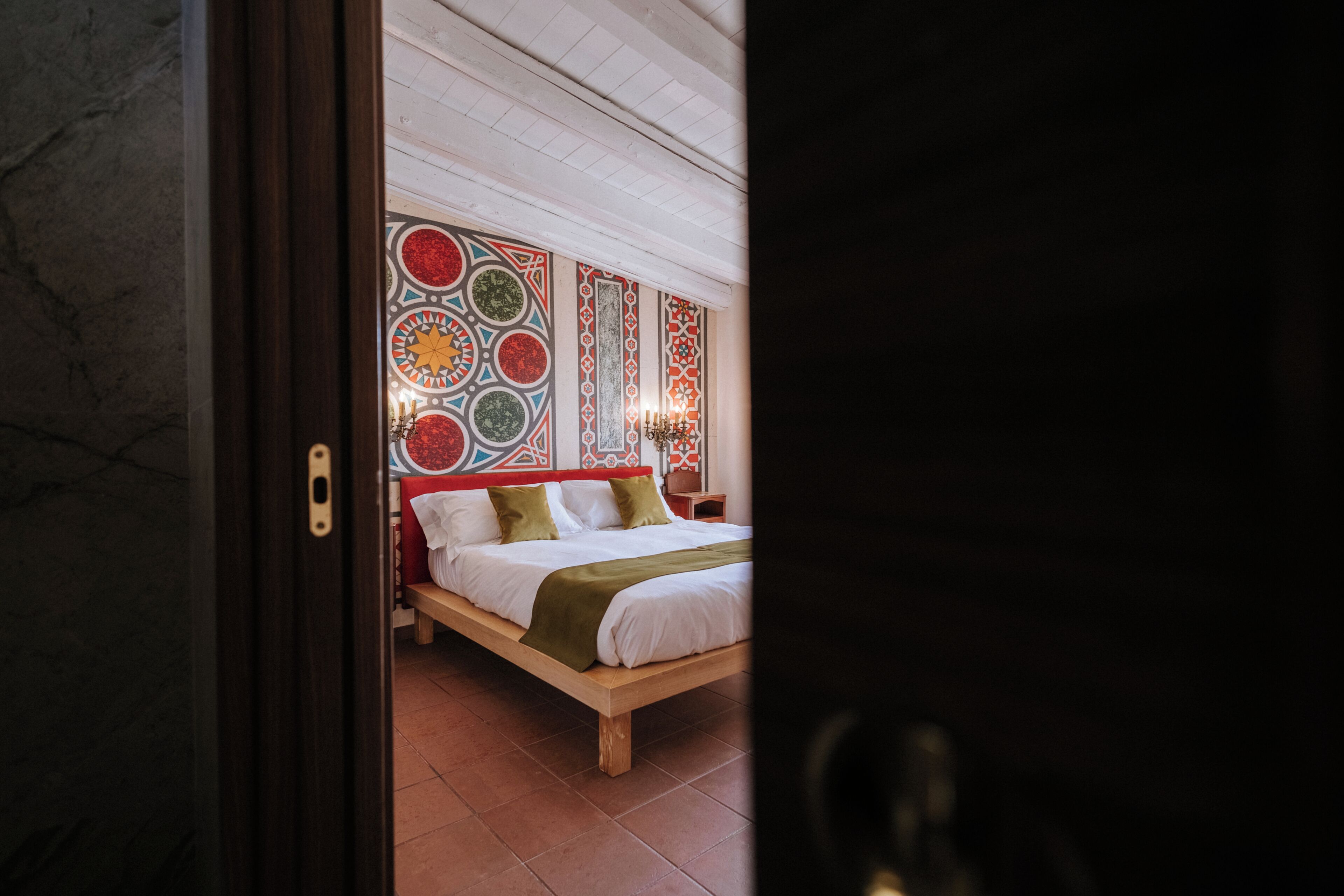 Une chambre avec un lit en bois, une tête de lit à motifs et un sol carrelé.