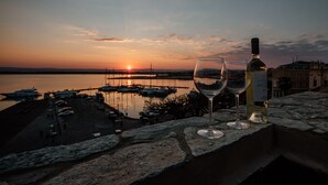 Zonsondergang vanaf een stenen balkon met twee wijnglazen en een fles.