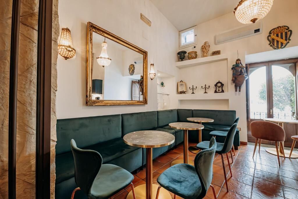 A cozy interior with a green sofa, round tables, and chairs, a large mirror, and decorative items on the walls.