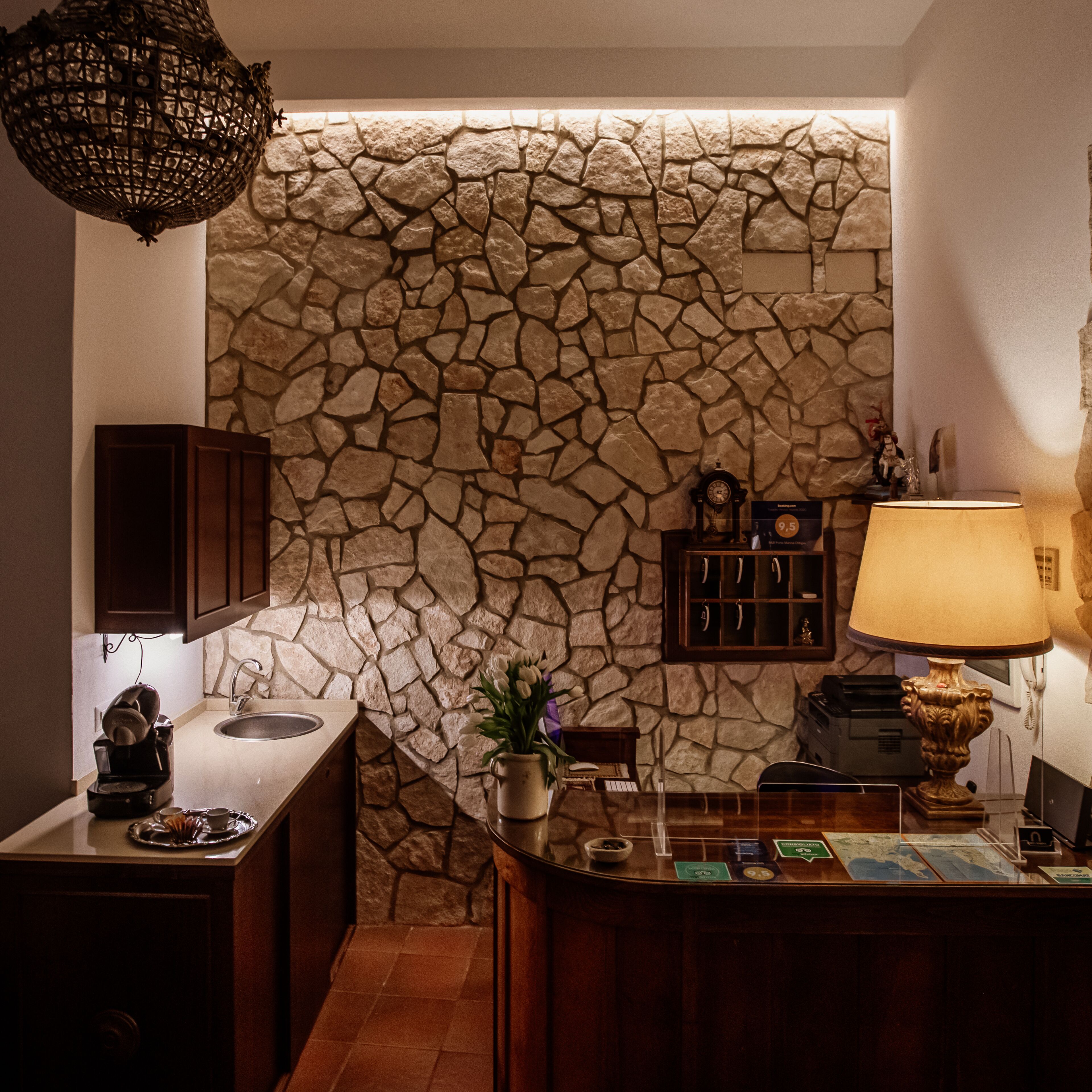 Una cocina con pared de piedra, armarios de madera, una cafetera, un lavamanos, una lámpara y un mapa sobre la encimera.