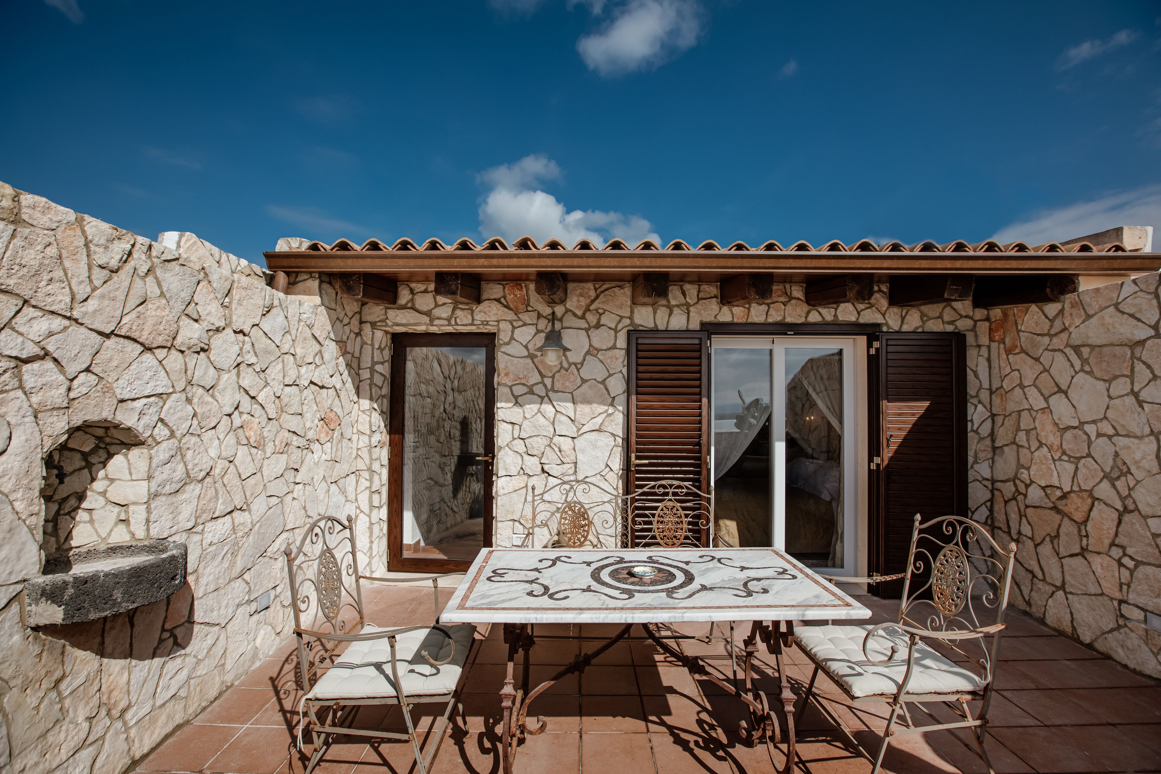 Un edificio de piedra con techo de tejas, una pared de piedra y un patio con mesa y sillas.