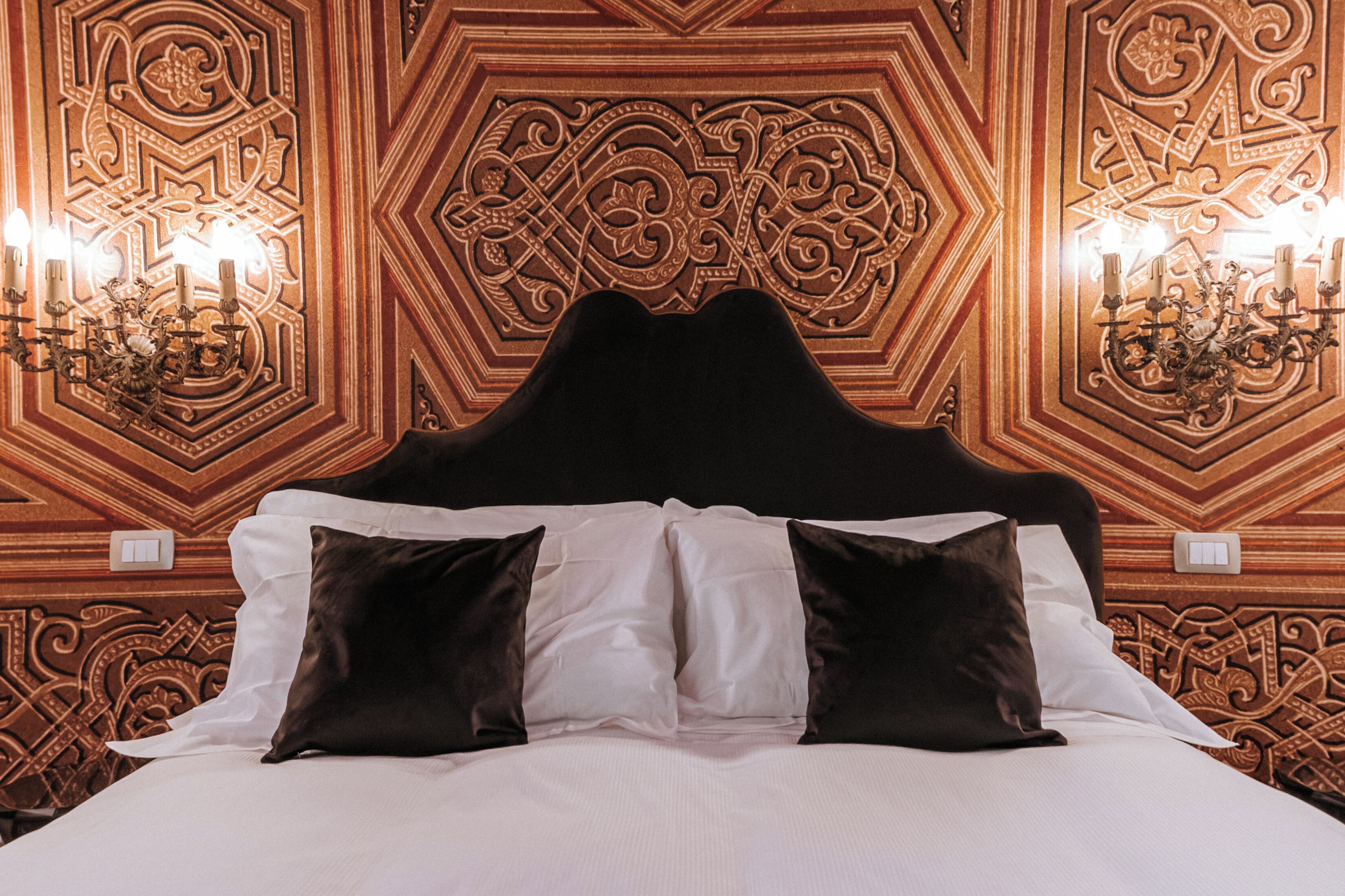 A bed with a black headboard, white and brown pillows, and a geometric patterned wall behind.