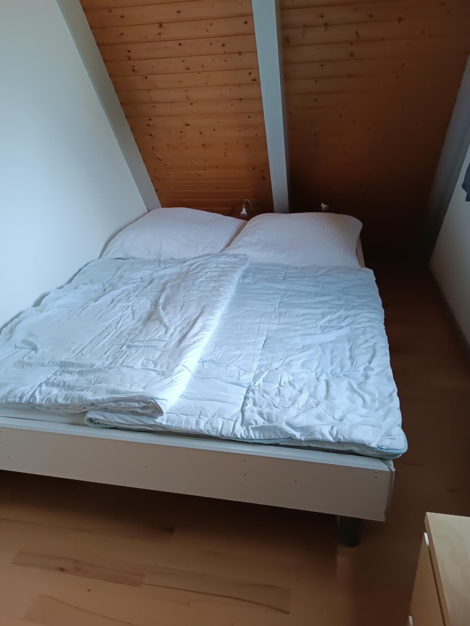 Een eenpersoonsbed met witte beddengoed in een kamer met houten balken aan het plafond.