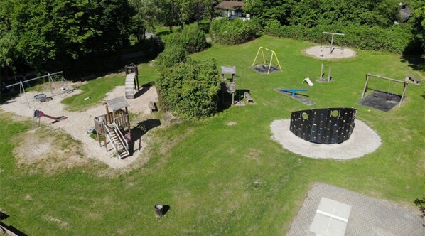 An aerial view of a park with playground equipment, a wooden structure, and a circular climbing area. - Holiday park - Winnetou (Waldbrunn)