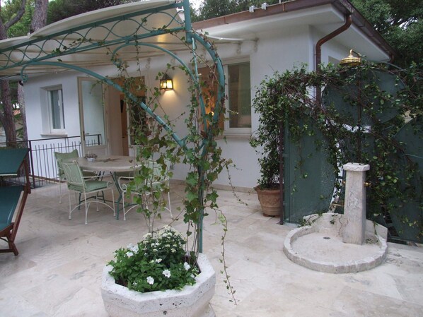 Une terrasse avec une table et des chaises, un pot de fleurs et une fontaine en pierre.