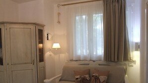 A room with a beige sofa, a white armchair, a wooden wardrobe, a lamp, and a window with curtains. - Apartment- Iris - One Bedroom Apartment, Sleeps 4 (Marina di Castagneto Carducci)