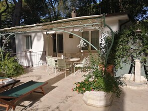 Une terrasse extérieure couverte, dotée d’une table et de chaises, et agrémentée de plantes en pot et d’une nichoir.