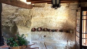 A rustic stone interior with a wooden beam ceiling, a stone wall with a large hole, and a row of small pottery items. - Hotel Hort De Fortunyo (Arnes)