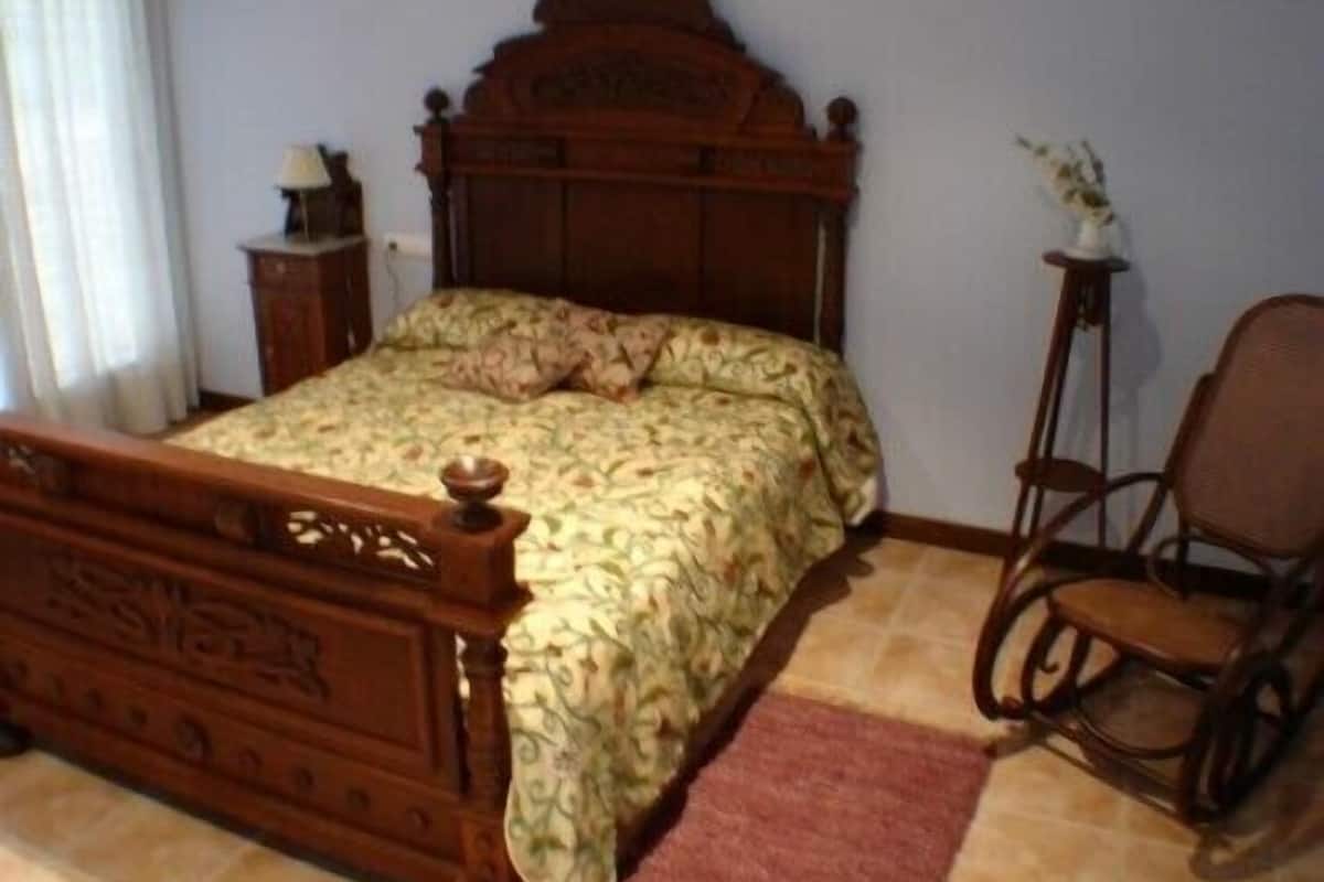 A bedroom with a wooden bed, a nightstand, a chair, and a small table with a lamp.