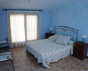A bedroom with a bed, two bedside tables, a chair, and a window with curtains.