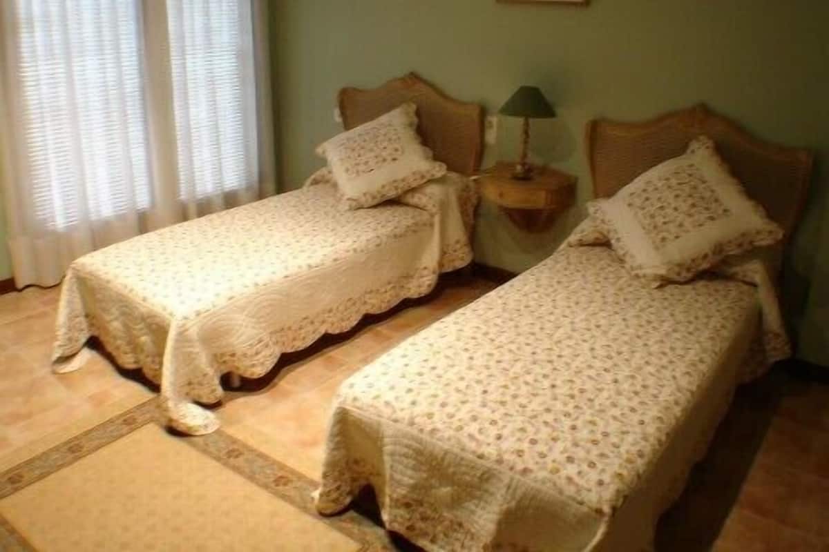 Two single beds with matching headboards and footboards, a bedside table with a lamp, and a window with blinds.