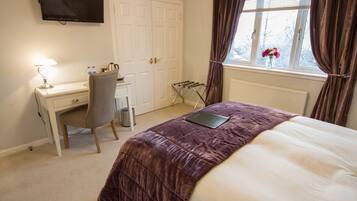 A hotel room with a bed, a desk, a chair, a TV, and a window with curtains.