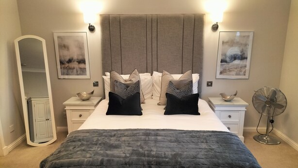 A bedroom with a large bed, two bedside tables, a mirror, wall art, and a standing fan. - Springfield Lodge B&B (Stirling)