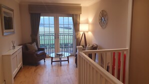 A living room with a sofa, a glass coffee table, and a lamp. There is a balcony with a view of the outdoors. - Springfield Lodge B&B (Stirling)