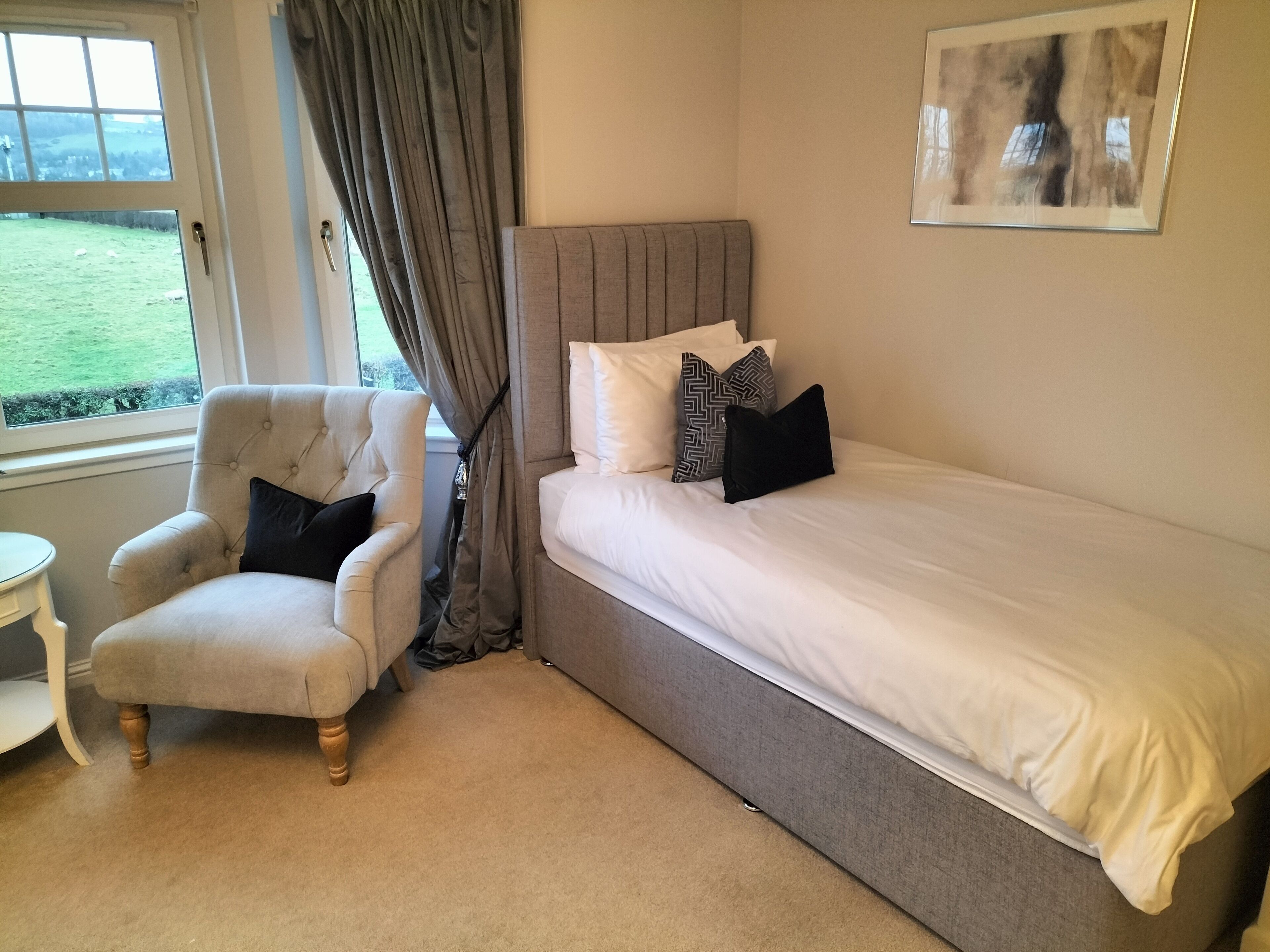 Une chambre à coucher avec un lit, une chaise, une petite table et une fenêtre avec des rideaux.
