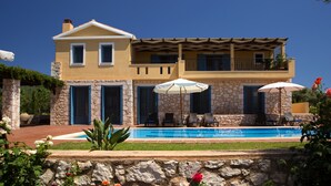 A two-story house with a swimming pool, stone facade, and outdoor seating area with umbrellas. - Villas Armeno (Lefkada)