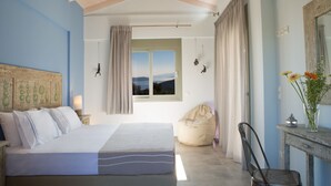 A bedroom with a bed, a bean bag, a chair, a window with curtains, and a view of the outdoors. - Villas Armeno (Lefkada)