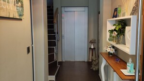 Un pasillo con una lámpara moderna, una escalera y un mostrador de recepción con una planta y un letrero de bienvenida.