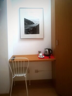A small room with a wooden desk, a white chair, a framed photograph on the wall, and a kettle on the desk. - Hotel Dabeleira (Valdes)