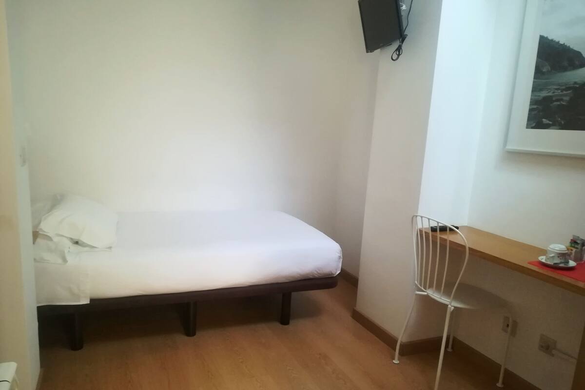 A small, compact room with a single bed, a desk, and a chair.
